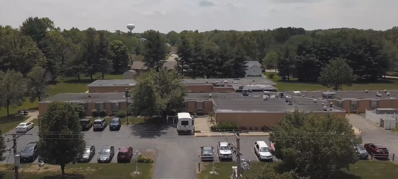 Aerial view of a single-story nursing and rehabilitation facility with a front parking lot, surrounding trees, and nearby houses.