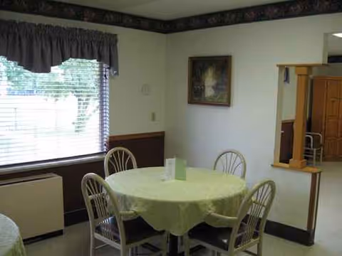Round table with a light green tablecloth and metal chairs in a senior living dining room.