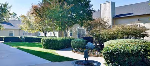 Exterior view of Bedford Estates Senior Living with manicured hedges and a person.