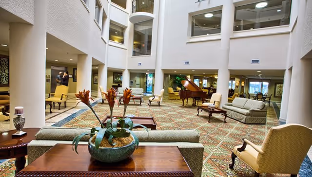 Spacious multi-story atrium lounge with sofas, chairs, a grand piano, and decorative plants.