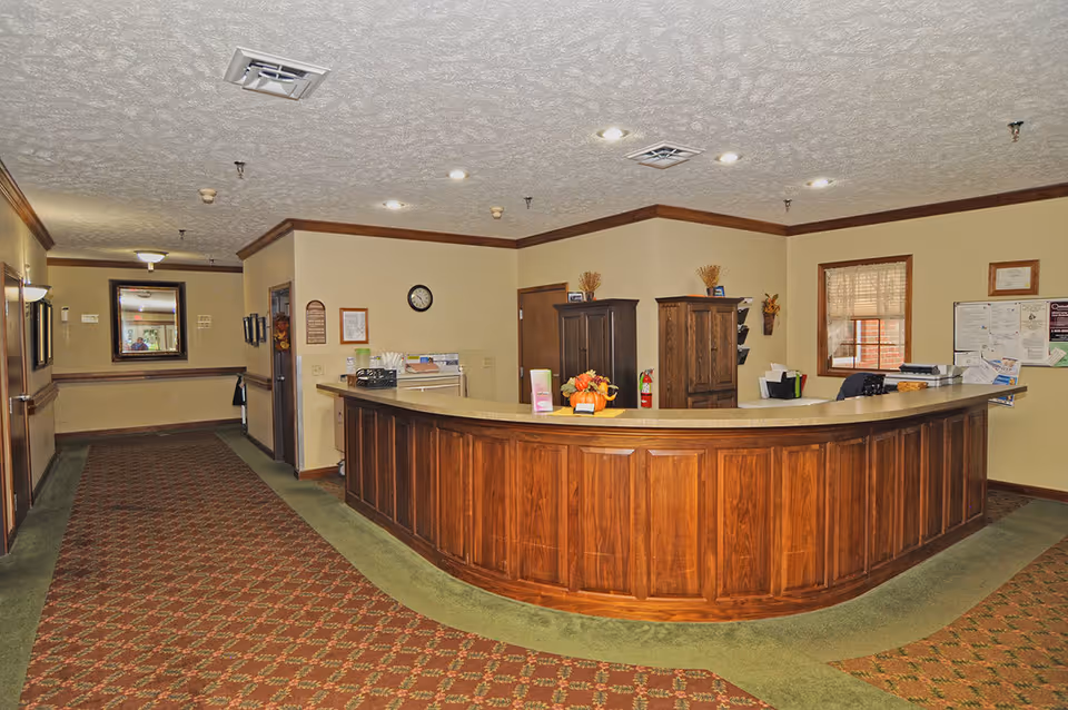 Curved wooden reception desk and lobby area with a hallway in an assisted living facility.
