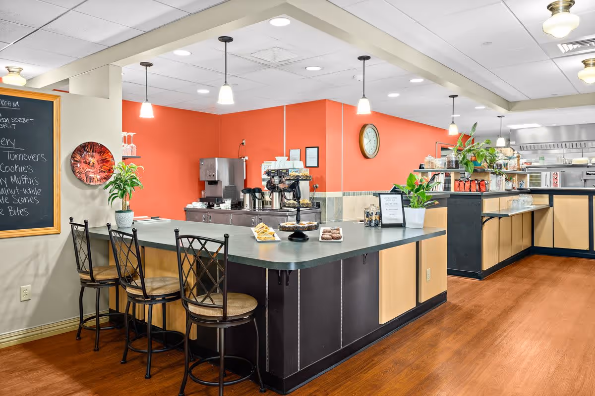 Bright dining/cafe area with a service counter, bar stools, coffee station, and pastries.
