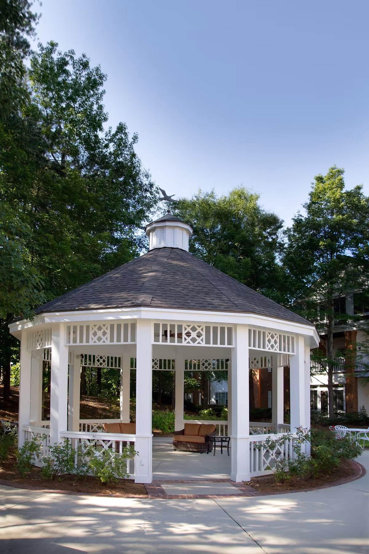 White wooden gazebo with seating in a tree-lined courtyard at Galleria Woods.