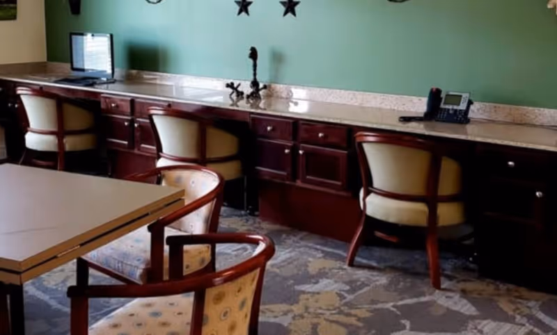 Seating area with a long built-in counter, swivel chairs, a computer monitor and telephone in a communal room with a green wall.