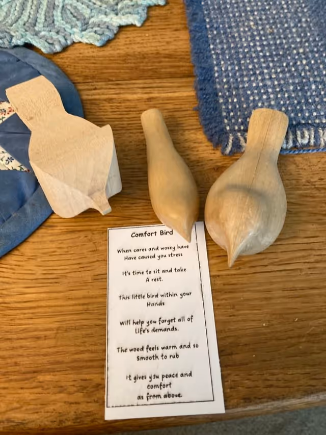 Three small wooden bird carvings and a printed 'Comfort Bird' poem on a wooden table with fabric placemats.