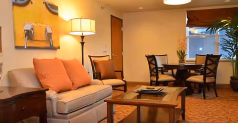 Warmly lit living area with a sofa, armchairs, coffee table and a round dining table near a window.