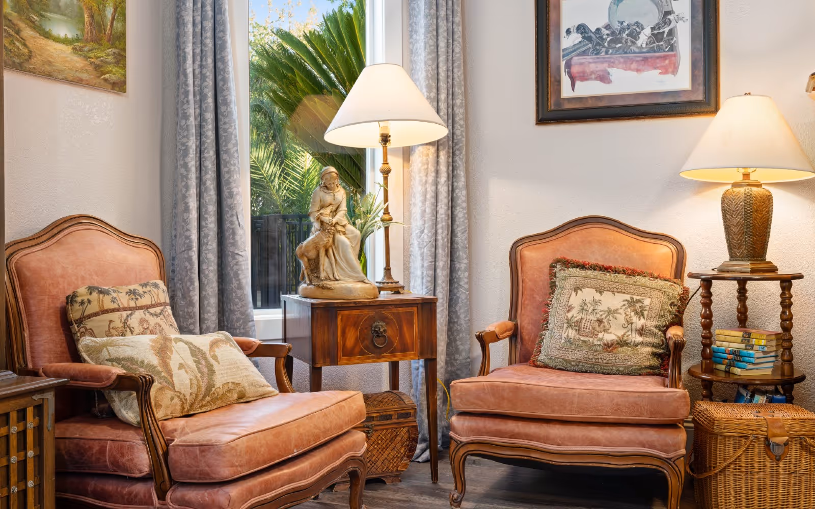 Two pink upholstered armchairs with patterned pillows flank a side table holding a statue and table lamp in a cozy sitting area.