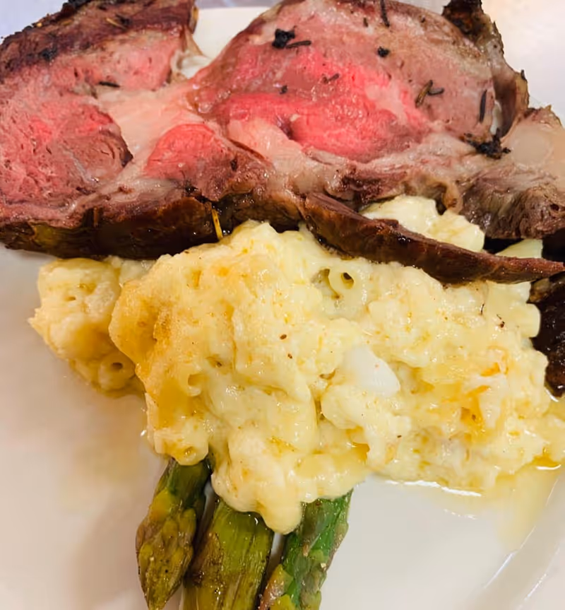 Plate with sliced medium-rare roast beef, creamy macaroni and cheese, and asparagus.
