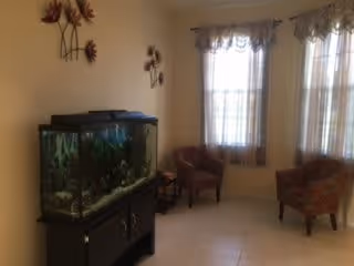 Small seating area with a large aquarium on a black stand, two upholstered chairs by tall windows, and floral wall decorations.