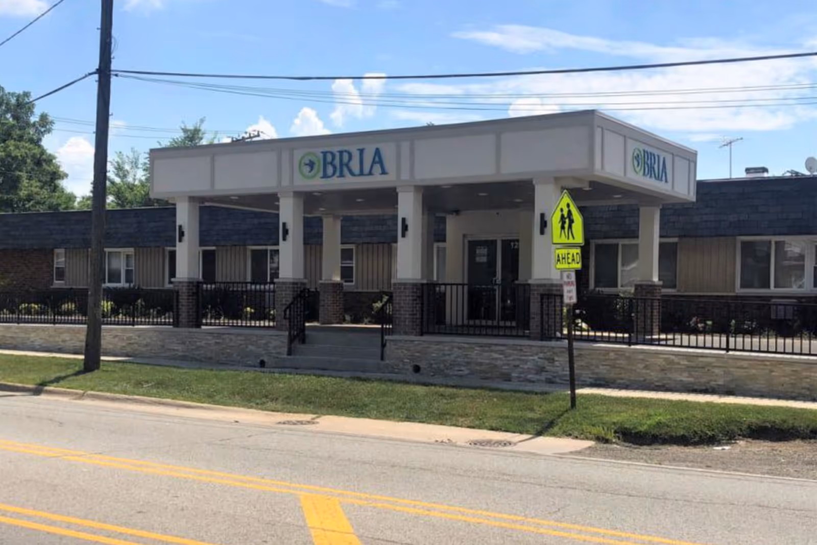 Front entrance of the BRIA of Chicago Heights building with a covered canopy, columns, and a pedestrian crossing sign in front.
