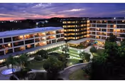 Dusk view of a multi-story senior living building surrounding a landscaped courtyard with pathways, a fountain, and illuminated windows.