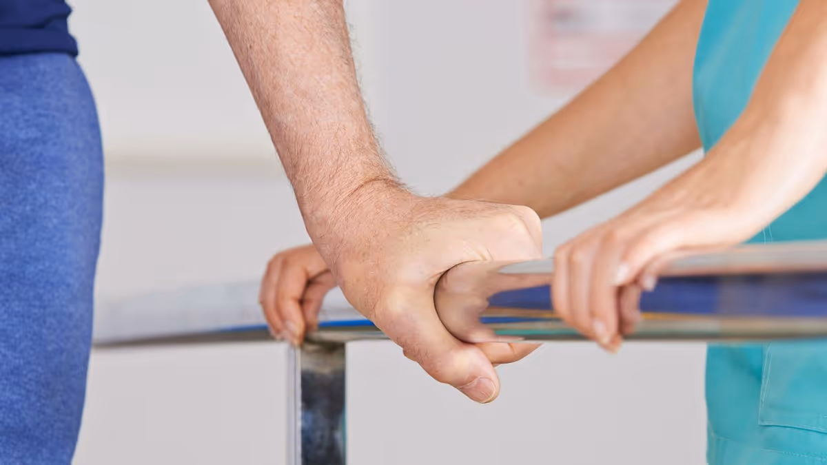 Close-up of two people holding onto a parallel bar, one person assisting the other, likely during a physical therapy or rehabilitation session.
