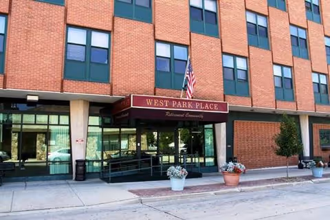 Exterior of a brick senior living building with glass entrance doors and planters.