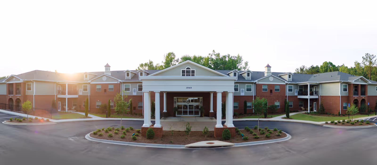 Front exterior of a two-story senior living building with a columned porte-cochère, circular driveway, and landscaped grounds.