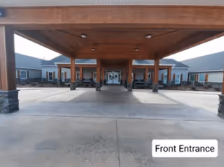 Covered main entrance with a wooden porte-cochere, stone-clad columns, and double glass doors.
