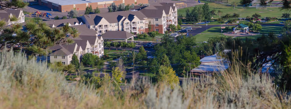 Aerial view of St. John’s United senior living facility showing multiple residential buildings surrounded by trees, green lawns, and outdoor recreational areas including a playground and walking paths.