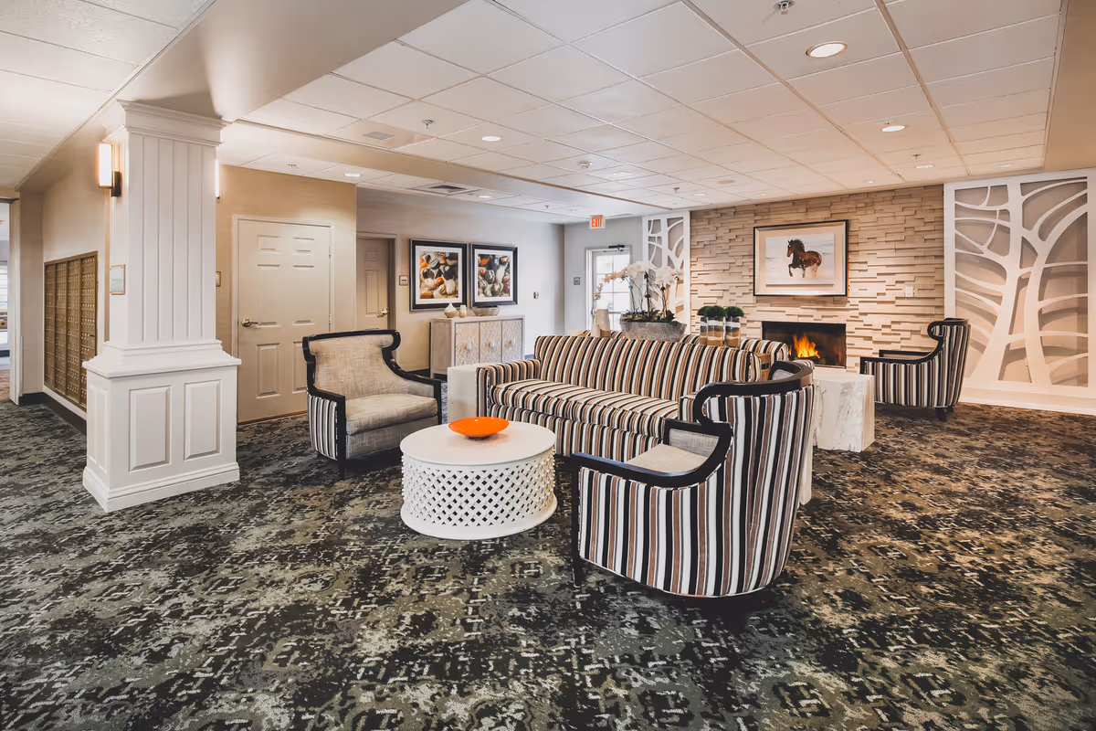 Comfortable lounge with striped sofas and armchairs arranged around white coffee tables in front of a fireplace.