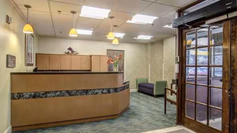 Curved wooden reception desk in a softly lit Manor Care lobby with seating and glass doors.