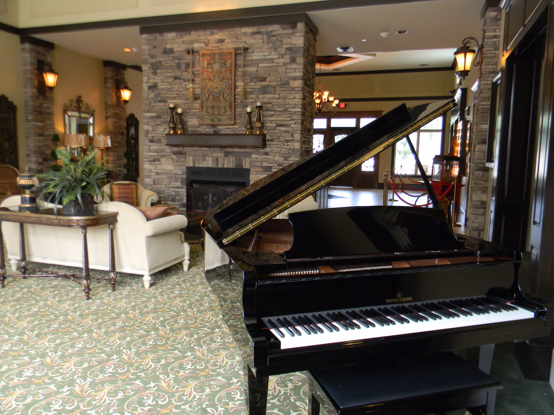 Lobby-style living room with a black grand piano in the foreground, sofas and a stone fireplace in the background.