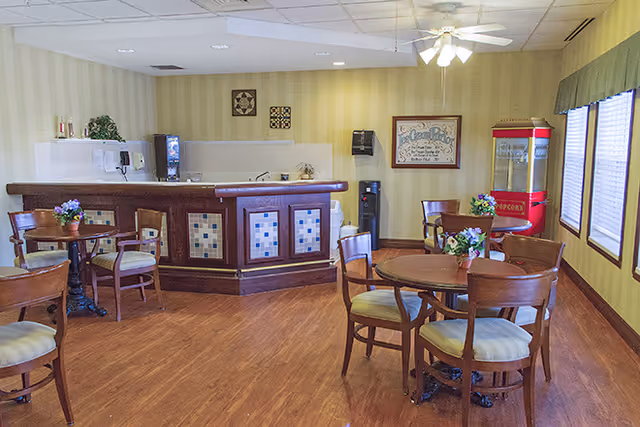 Communal dining area with round wooden tables and chairs, a service counter, and a popcorn machine.