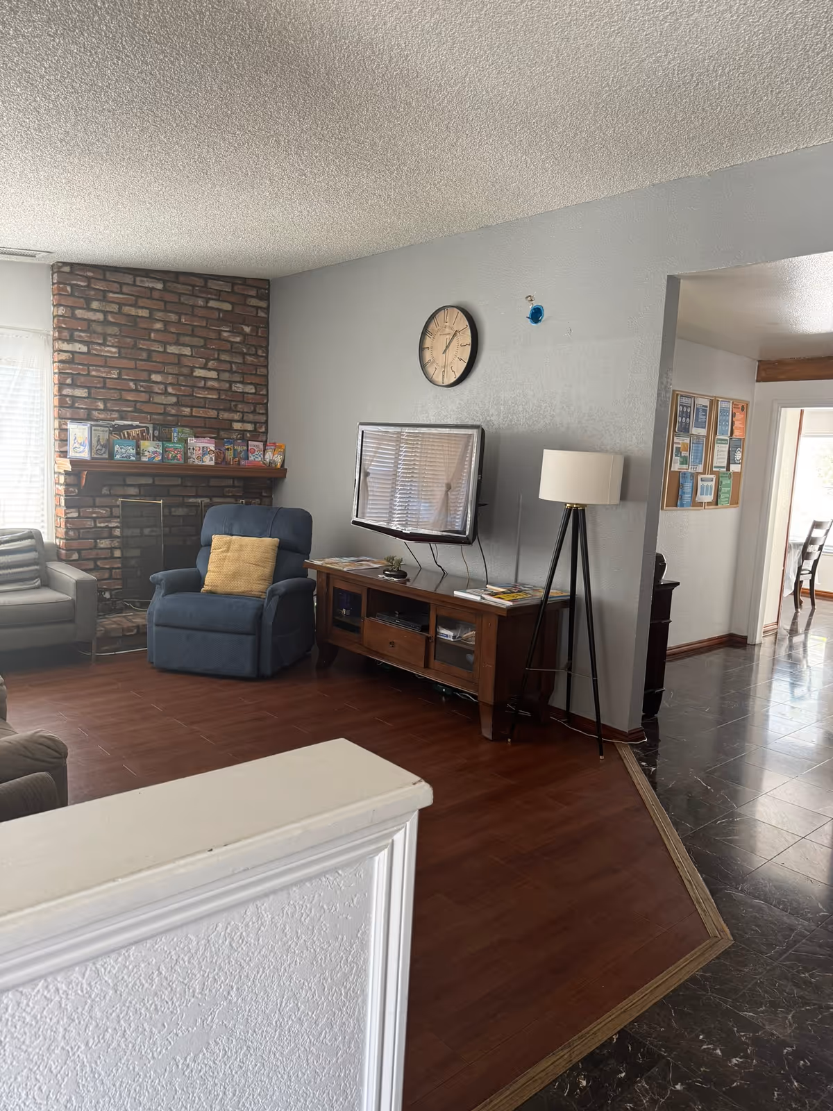 Living room with a brick fireplace, a blue recliner, wall-mounted TV on a gray wall, wooden media console, and a floor lamp.