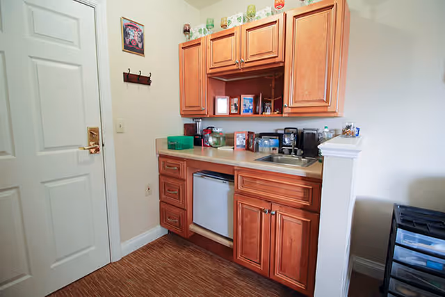 Small kitchenette area with wooden cabinets, a countertop sink, mini fridge, and small appliances.