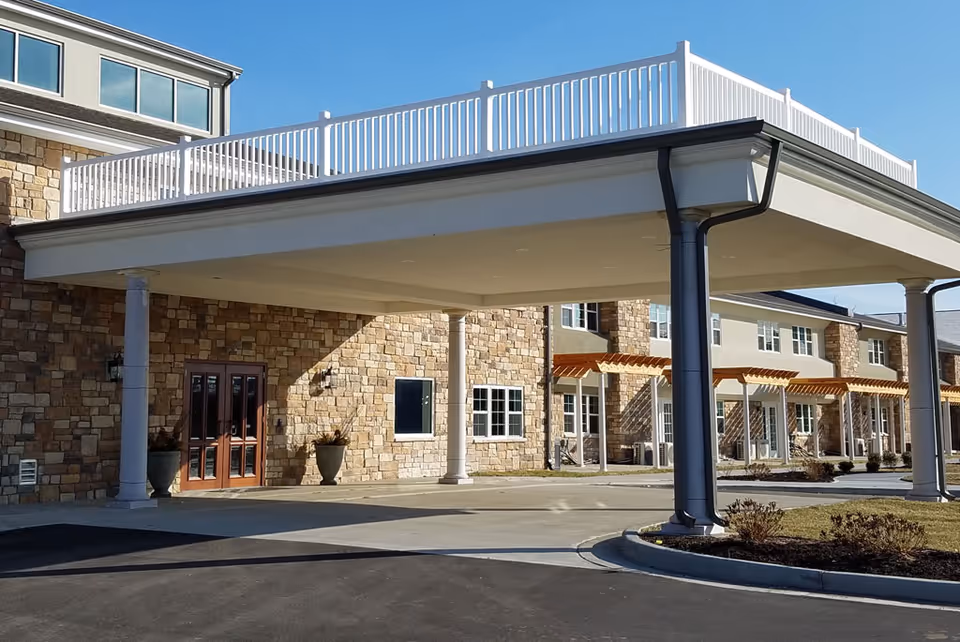 Covered porte-cochere entrance of a stone-faced senior living building with columns and upper railing.