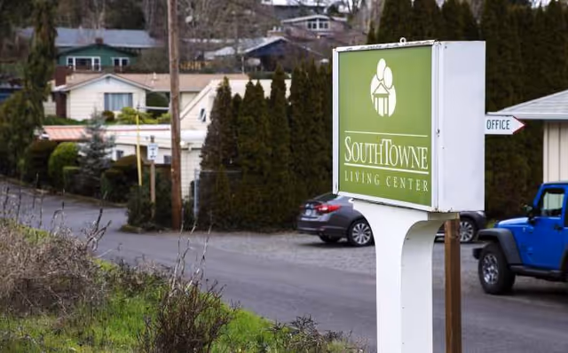 Exterior view of a green SouthTowne Living Center sign beside parked cars.