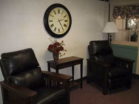 Two black leather chairs flank a small table with a vase and clock on the wall.