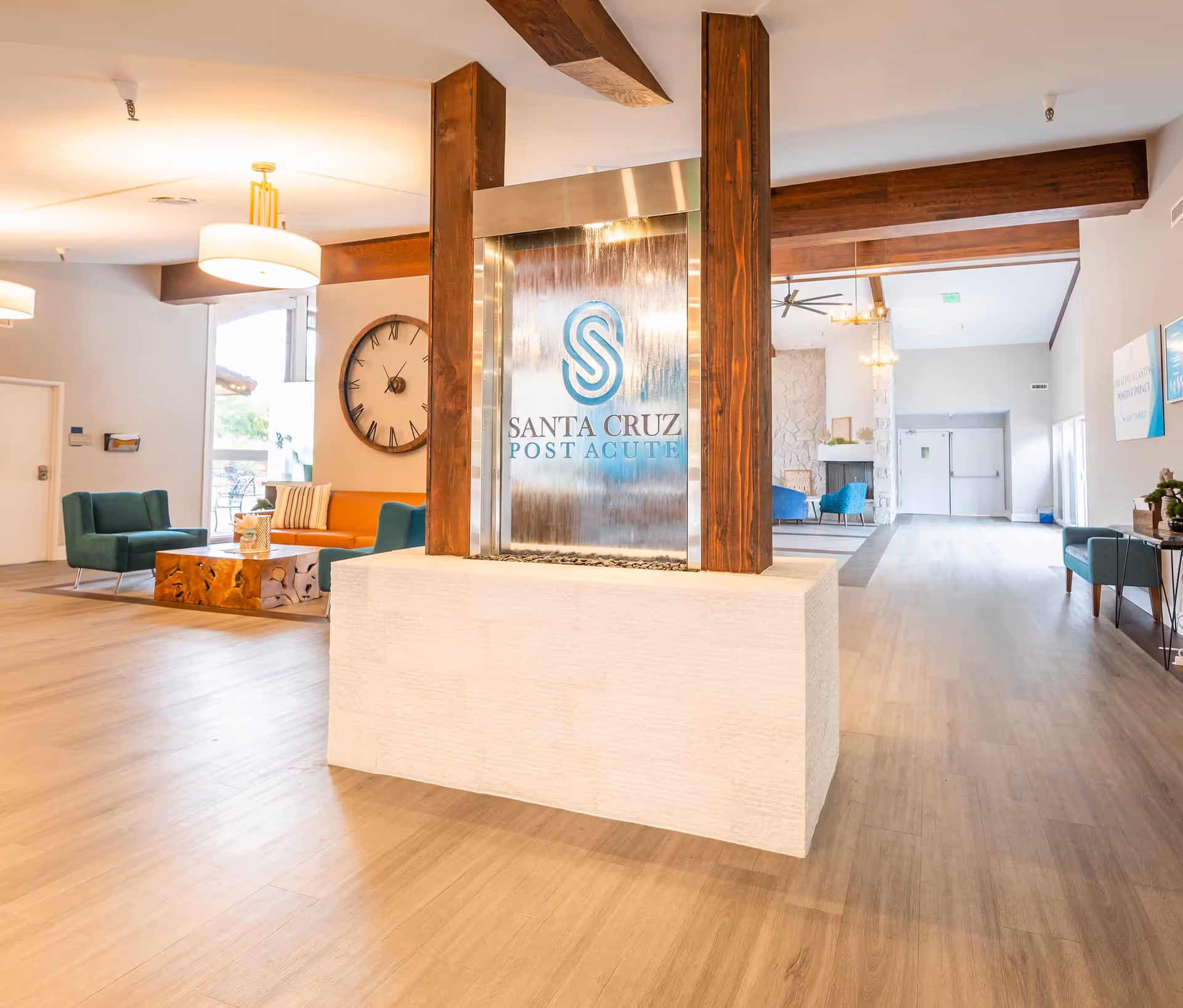 Lobby of Santa Cruz Post Acute featuring a central glass waterfall with the facility logo, seating areas, and exposed wooden beams.