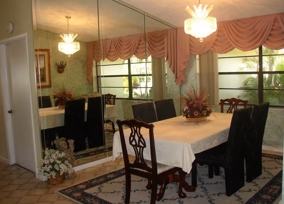 Formal dining room with a central table, mirrored wall, pink drapes, and chandeliers.