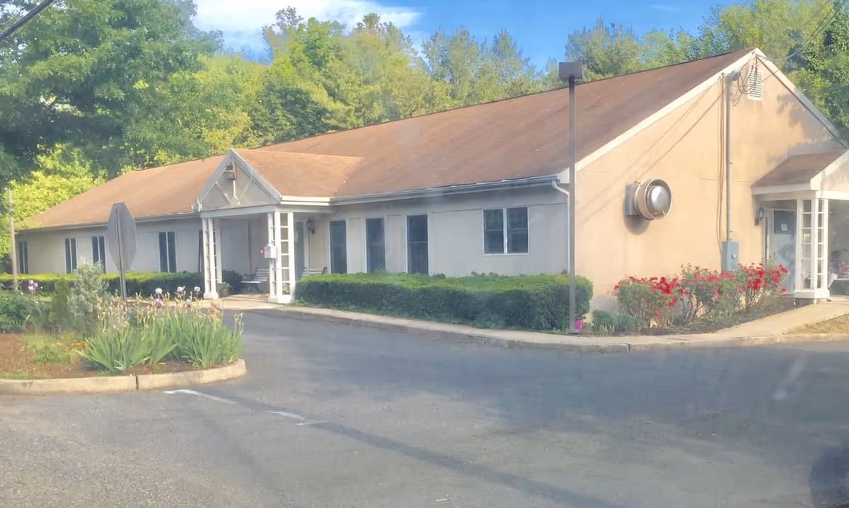 Single-story senior living building with a sloped roof, two covered entrances, and landscaped driveway in front.