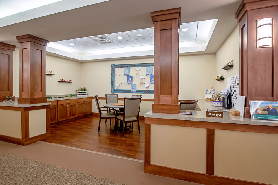 Interior common area with a reception counter, wooden columns and a small table with chairs against a light-colored wall.