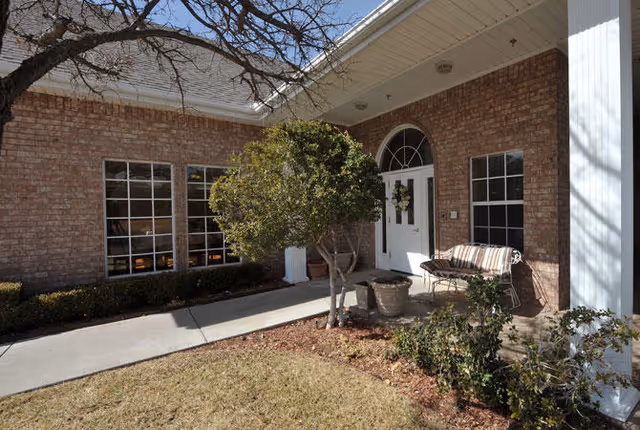 Brick front entrance with a white double door and arched transom, a bench, potted plants, and a small tree by the walkway.