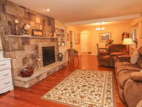 Cozy living room with stone fireplace, hardwood floors, and plush sofas in a senior facility.