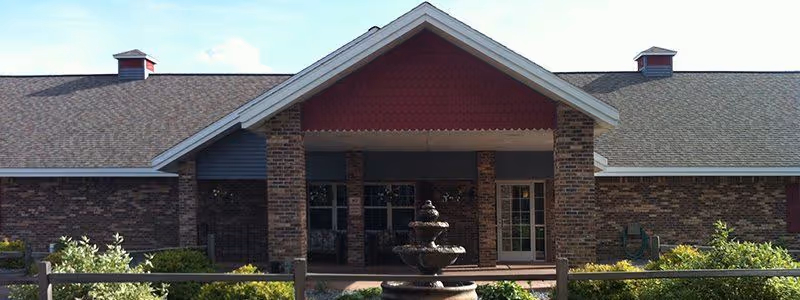 Entrance of a brick senior living building with a covered porch and a tiered fountain in front.