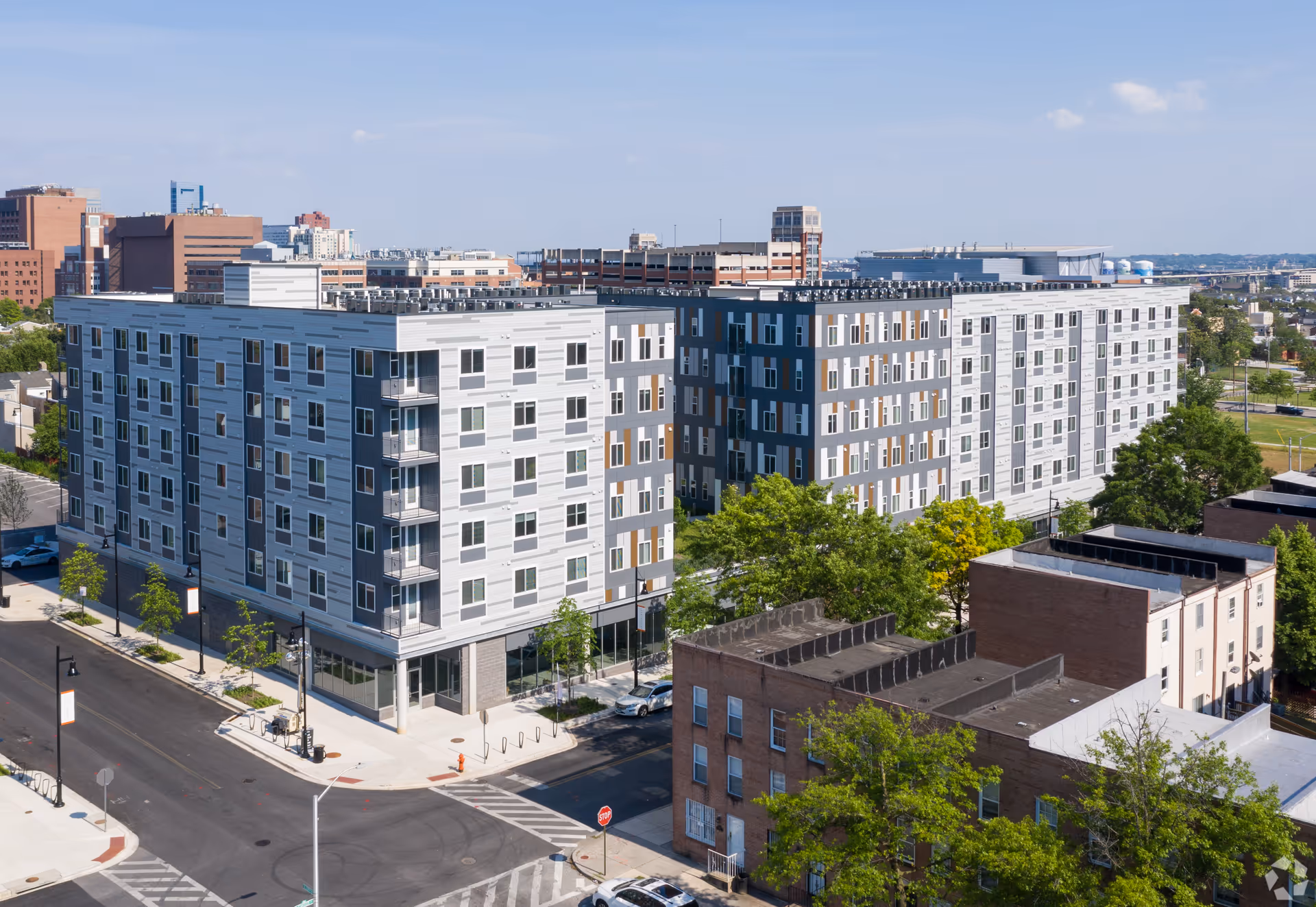 Aerial view of a modern six-story residential building occupying a city block, surrounded by streets, trees, and neighboring buildings.