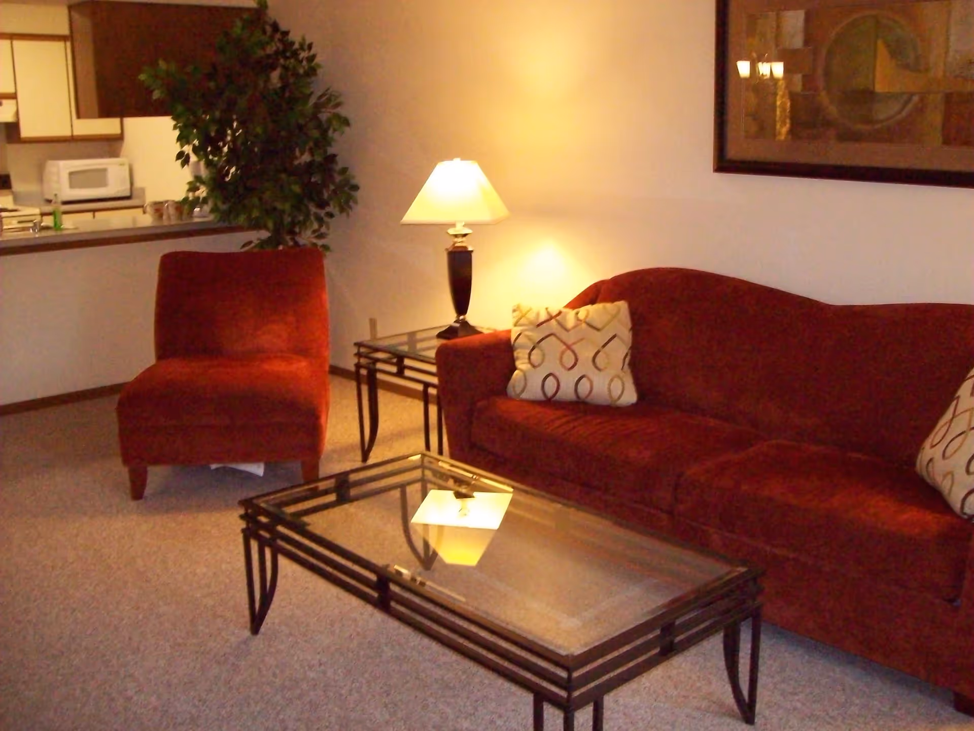 Cozy living room with a red sofa and chair, glass coffee table, side table and lamp.
