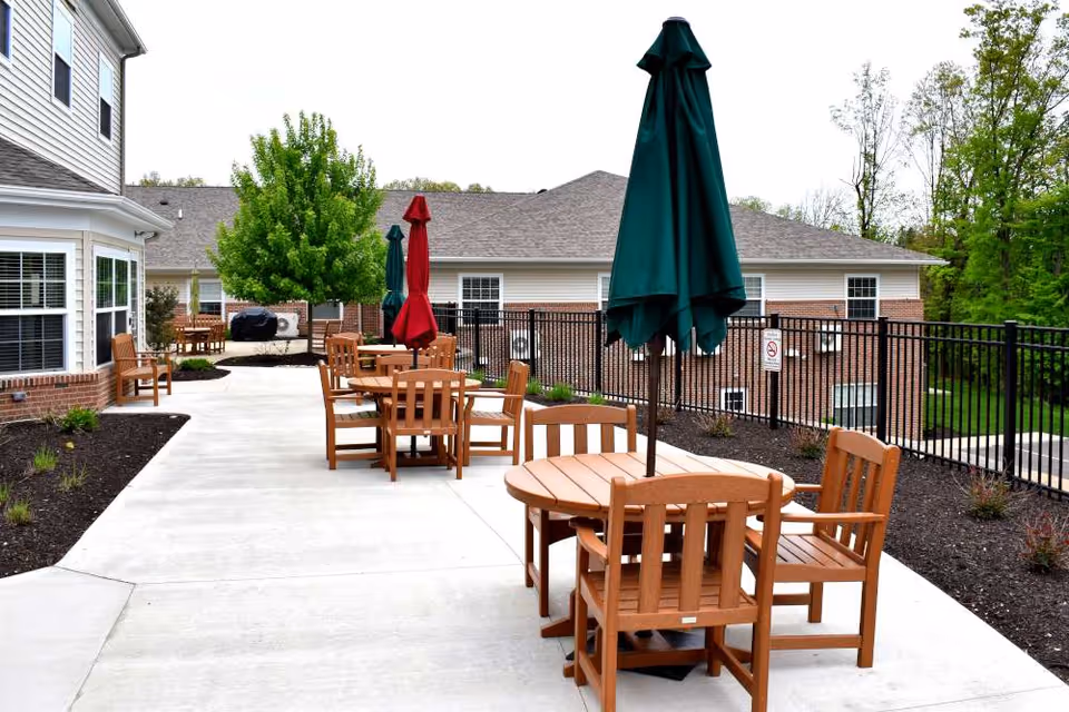 Outdoor patio area at Danbury Wooster with wooden tables and chairs, each table featuring a closed umbrella. The patio is surrounded by a black metal fence, with buildings and trees in the background.