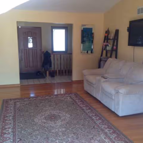 Living room with beige walls, wooden floor, couch, rug, and wall-mounted TV.