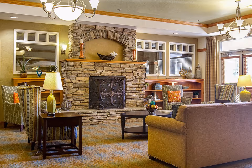 Cozy common living room with a stone fireplace, sofas, armchairs, lamps, and a coffee table.