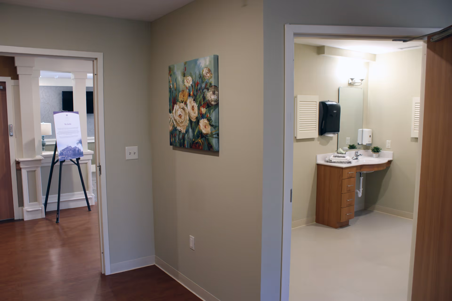 Interior hallway with a floral painting and an open doorway revealing a bathroom sink and vanity.