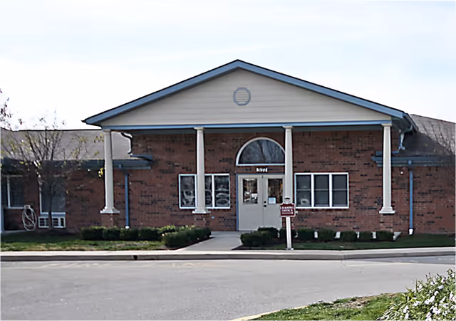 Single-story brick building with a gabled portico, white columns, and a central entrance door.