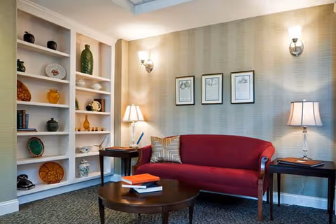 Cozy sitting area with a red sofa, round coffee table, built-in shelving with decorative items, and table lamps.