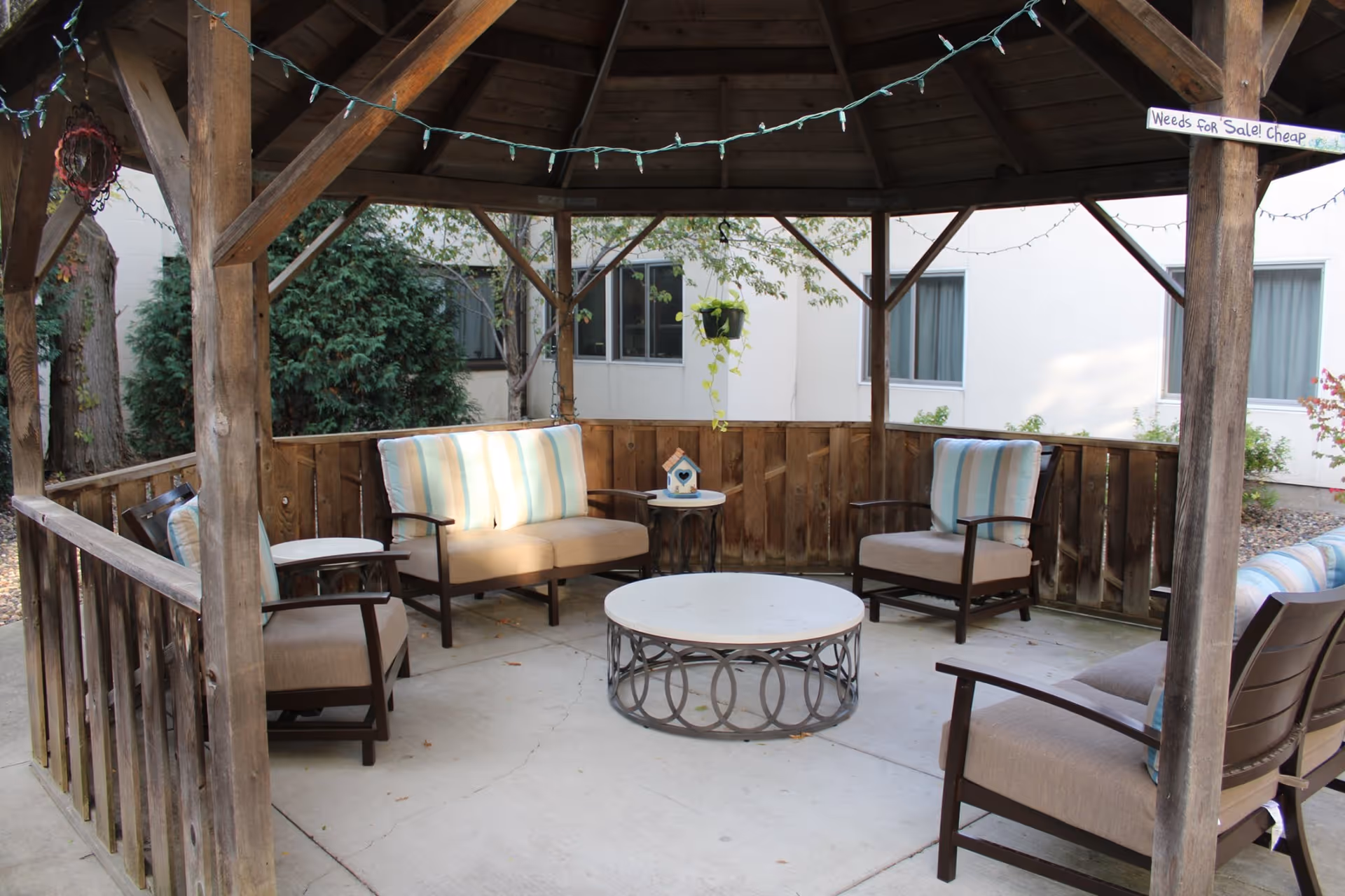 Wooden gazebo with cushioned outdoor seating and a round coffee table in a courtyard.