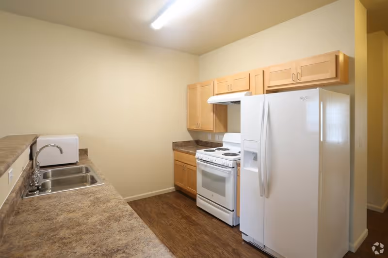 Small apartment-style kitchen with white refrigerator and stove, wooden cabinets, a double sink and laminate countertops.