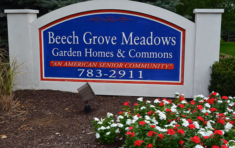 Entrance sign for Beech Grove Meadows Garden Homes & Commons, an American senior community, surrounded by mulch and red and white flowers.