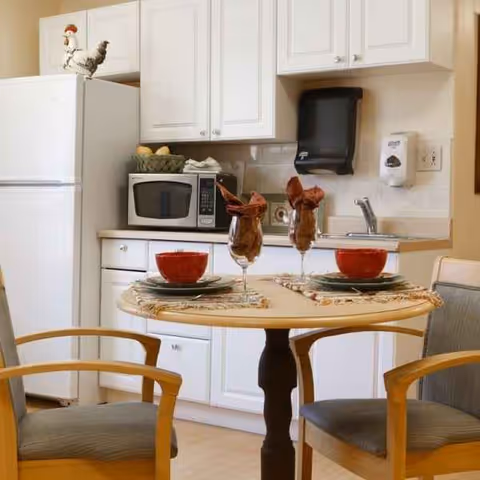 Round dining table with two place settings in a white kitchenette beside a fridge.