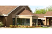 Brick senior living facility exterior with large glass windows and landscaped entry.
