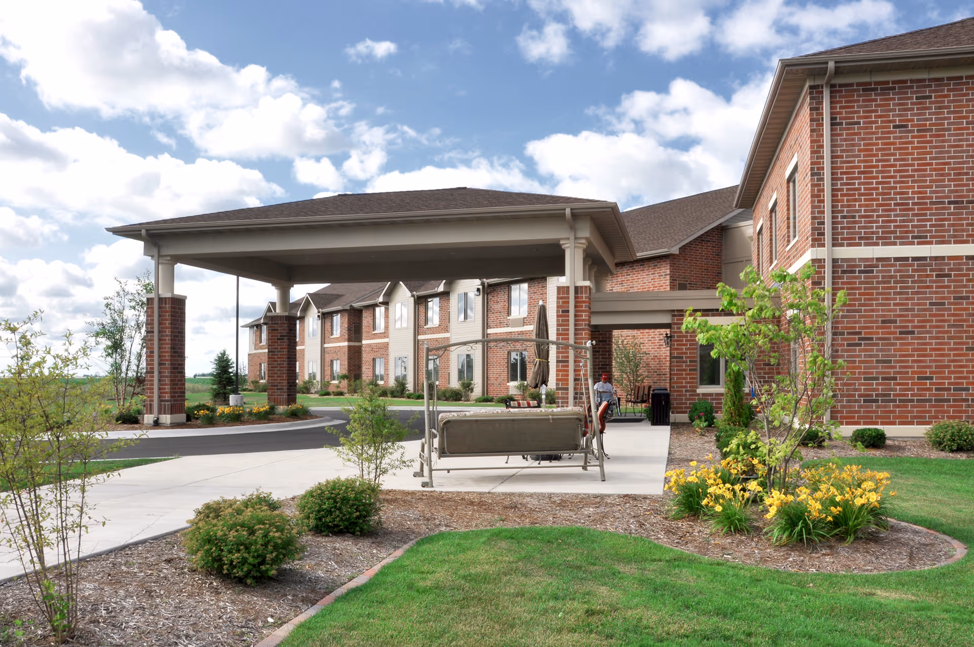 A senior living facility entrance with lush landscaping and outdoor seating.